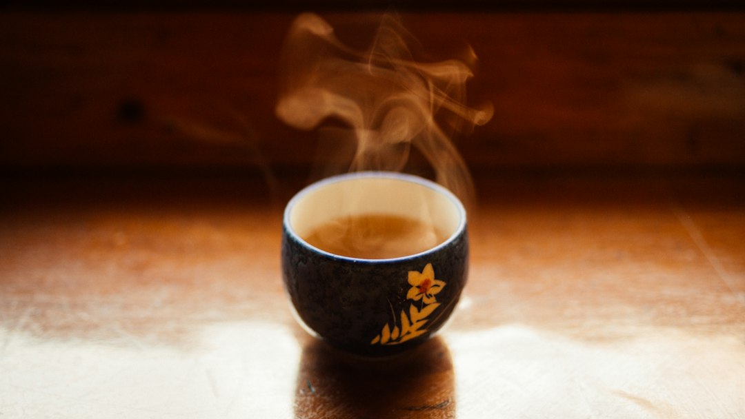 Steam rising from a small cup of tea on a wooden table